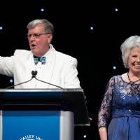 On the Enrichment stage, President Tom Haas makes the Laker hand gesture while Marcia Haas waves.